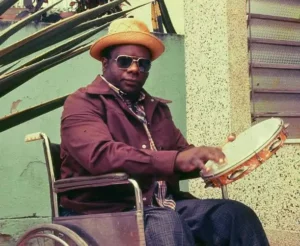 Candeia compositor de Preciso Me Encontrar tocando pandeiro em cadeira de rodas