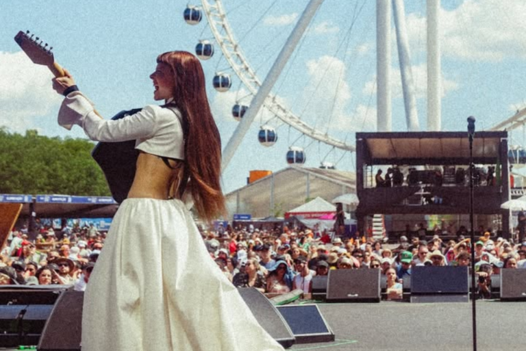 Cantora Júlia Mestre performando em um festival de música ao ar livre com roda gigante ao fundo