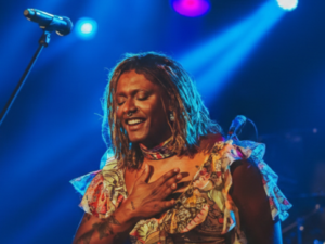 Liniker no palco com a mão no peito e os olhos fechados em gesto de agradecimento ao público